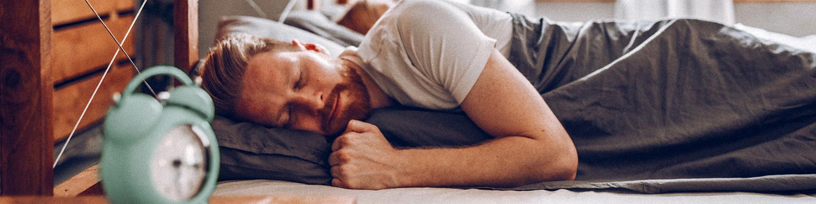 Man ligt te slapen in bed met wekker op nachtkastje