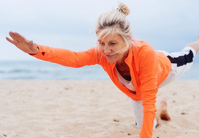 Oudere vrouw doet yoga op het strand